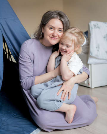Happy family smiling beautiful mom and her cute little daughter with blonde hair embracing and...