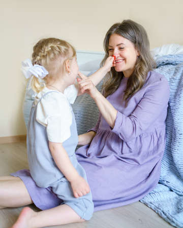 Young loving parent mother playing with little girl daughter, touching each others nose, having fun...