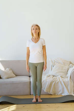 Active lifestyle on retirement. Calm focused senior woman in home wear standing in mountain pose on...