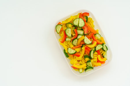 View from above on vegan cold pasta salad with fresh veggies cucumber and bell peppers in plastic container isolated in grey background with copy space for text. Vegetarian food conceptの写真素材