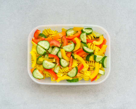Top view on lunch box with vegetarian healthy vegetable cold pasta salad with cucumber and bell peppers isolated in grey background. Vegan recipes conceptの写真素材