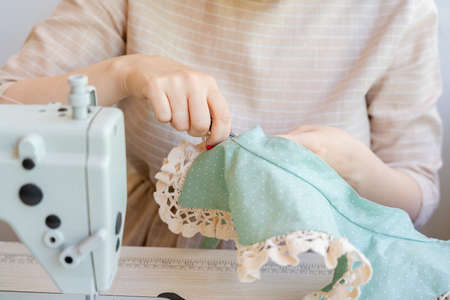 Professional seamstress making vintage lace collar at atelier, cropped shot. Female fashion designer holding fabric and scissors while working at workplace with sewing machine. Creative hobby conceptの写真素材