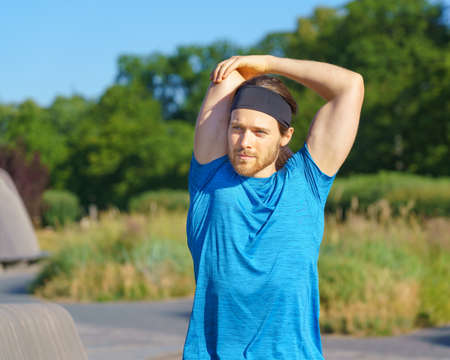 Young sportive active man in sportswear warming up outdoors in nature in morning time, handsome male sportsman preparing body muscles for running in green park. Sport and active lifestyle conceptの写真素材