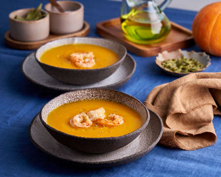 Pascetarian pumpkin and carrot cream puree soup with shrimps and herbs in bowl on blue linen tablecloth. Side view, close up, horizontal. Concept of eat less meat foodの写真素材