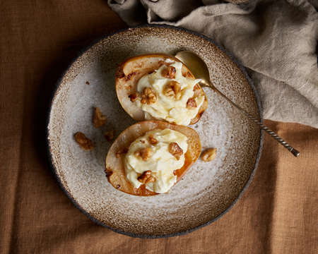 Top view of halved sweet grilled pears served on ceramic plate. Appetizing autumn dessert with walnuts and cream on top. Gourmet vegetarian cooked meal on wooden backgroundの写真素材