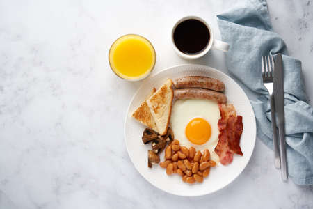 Horizontal top view of classic rustic delicious irish cuisine meal. Fried eggs, grilled sausages, roasted mushrooms, toast, kidney beans, hot coffee and fresh orange juice. Light background copy spaceの写真素材