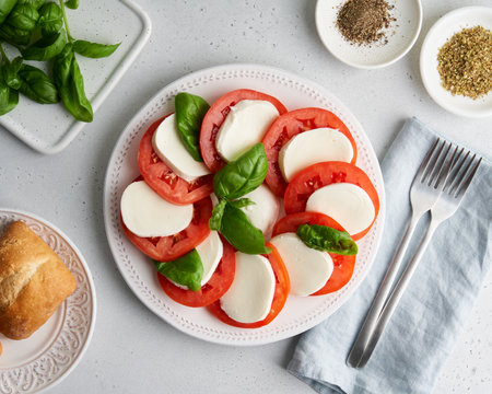 Traditional recipe of italian caprese salad with sliced tomatoes, mozzarella, basil, oregano, pepper, ciabatta. Horizontal flat lay of delicious mediterranean appetizer. Fresh vegetarian mealの写真素材