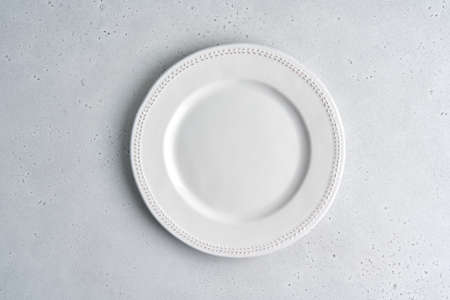 Empty white ceramic plate on light background. Clean tableware. Serving preparation. Novody, Above dishware. Cutlery set. Copy space, top view, horizontal, closeupの写真素材