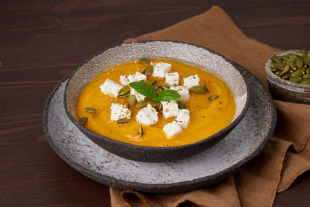 Traditional pumpkin cream soup with feta cheese. Rustic home made dish of smeared pumpkin, spices and basil. Fall fresh seasonal dish on wooden background. Closeup, horizontal, side viewの写真素材