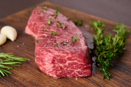 Raw marble striploin steak with thyme, rosemary, garlic, salt, pepper. Rustic beef tenderloin meat on wooden chopping board. Side view closeup horizontalの写真素材
