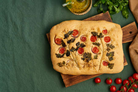 Food art. Focaccia, pizza, flat bread with vegetables, tradition italian cuisine. Flatbread with tomatoes, parsley and onion on dark green linen textile tablecloth. Top view, copy space.の写真素材