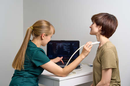 Young doctor doing ultrasound scanning of female patient. Nurse examining throat and blood vessels...
