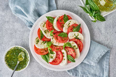 Delicious italian caprese salad with tomatoes, mozarella, basil leaves, olive oil. Pesto sauce ingredients pine nuts. European gourmet served meal. Horizontal, top viewの写真素材