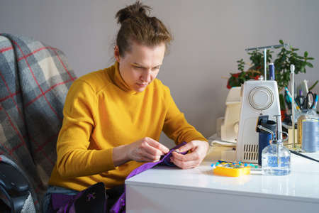Happy woman seamstress in casual wear sitting at her workspace with sewing machine at home and working on new fashion item purple corset, tailoring process. People and creative hobbies conceptの写真素材