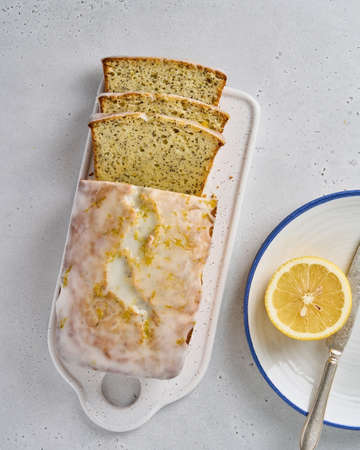 Flat lay of sliced lemon bread with poppy seeds, white frosting and citrus peel. Tasty sweet...