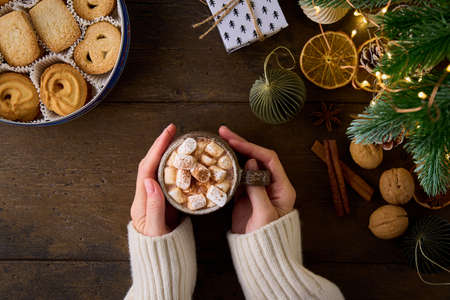 Anonymous female in white sweater holding cup of hot cocoa with marshmallows and grated chocolate on...