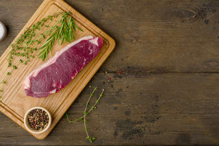 Raw striploin on wooden board with thyme, rosemary and pepper. Horizontal, above, copy spaceの写真素材