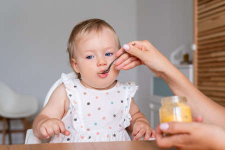 Anonymous mommy feeding little girl on highchair with spoon of vegetable porridge at homeの写真素材