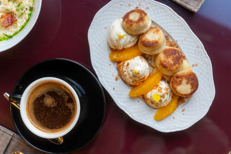 Sweet morning breakfast in cafe. Cheesecakes with cream and peaches, cup of dark coffeeの写真素材