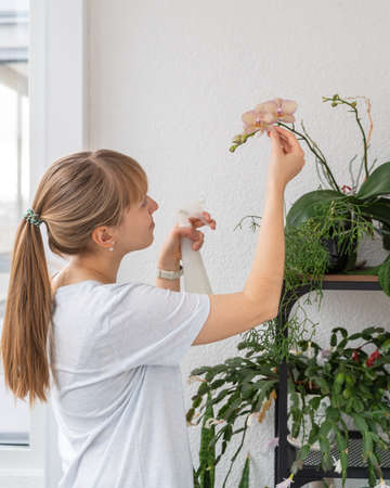 Portrait of young female taking care of houseplants and flowers on balconyの写真素材