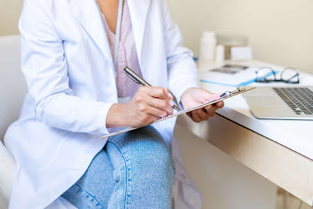 Anonymous doctor writing on clipboard. Filling patient form. Doing paperwork in medical clinicの写真素材