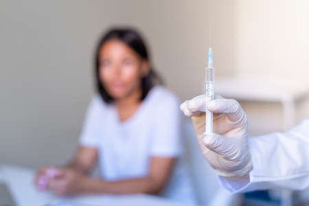Faceless doctor holding syringe before make virus vaccination to blurred female patientの写真素材