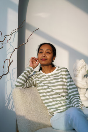 Thoughtful african-american female looking at window. Sunset natural light. Niksen lifestyle