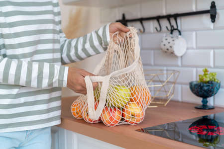 Anonymous woman buying groceries in eco bag. Sorting apples in kitchen. Zero waste shopping conceptの写真素材