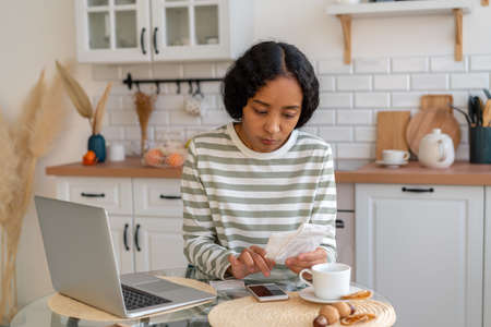 African-american female paying bills. Dealing with expenses on smartphone. Cutting back on spendingの写真素材