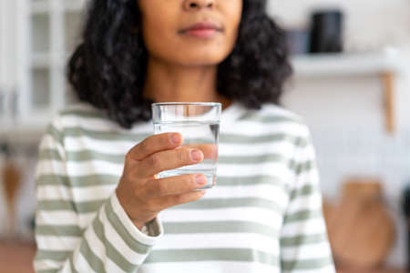 Faceless cropped african-american female drinking glass of water in kitchen. Refreshing start of dayの写真素材
