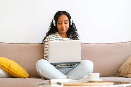 Attending online class from home. African-american student working on laptop, listening to lectureの写真素材