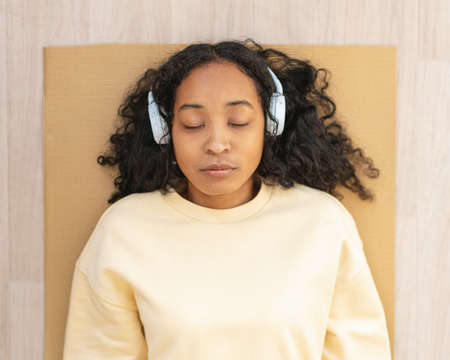 African-american woman in headphones resting on mat with closed eyes. Relaxing after exercisingの写真素材