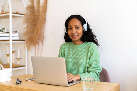 African-american female working on laptop in headphones. Listening to audio podcast onlineの写真素材