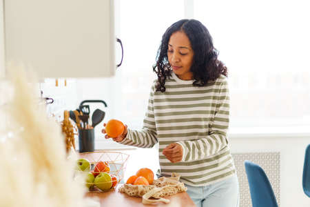 African-American female in kitchen sorting out apples and oranges after shopping in grocery storeの写真素材