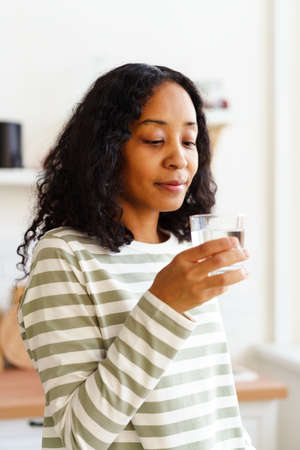 Smiling African-American female looking at glass of clear water on soft focused backgroundの写真素材