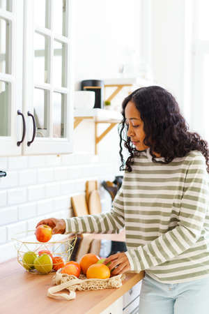 Smiling African-American female choosing healthy snack while sorting apples in kitchenの写真素材
