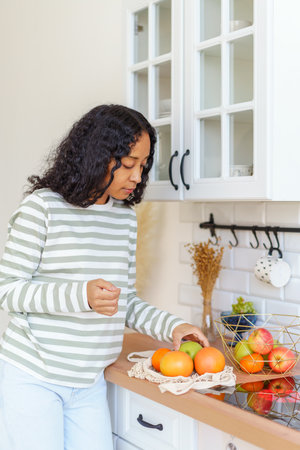African-American taking out apples and oranges after going at grocery store with eco-bagの写真素材