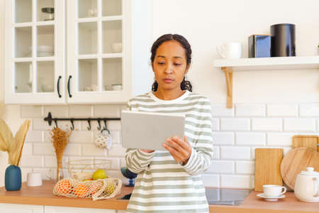 African-American female searching for recipe on tablet pc before cooking meal in kitchenの写真素材