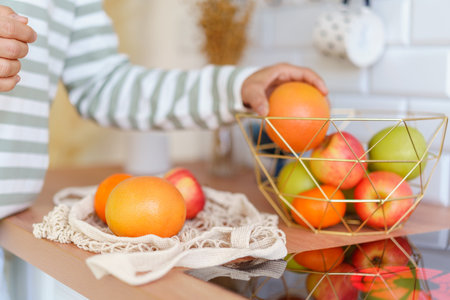 Faceless person grabbing ripe apple from fruit bowl on kitchen table. Sorting after grocery storeの写真素材