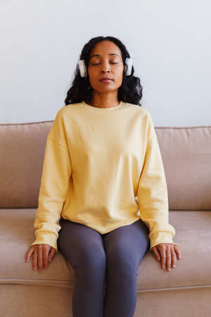 African-American female sitting on couch and listening to music in headphones. Breathing therapyの写真素材