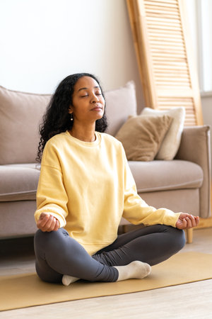 Young African-American female sitting in lotus yoga pose on mat in while meditating, verticalの写真素材