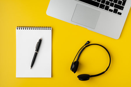 Contemporary workspace on yellow background. Notebook with pen, laptop and digital headsetの写真素材
