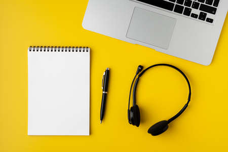 Modern office desktop. Blank notepad, pen, headset and laptop on yellow backgroundの写真素材