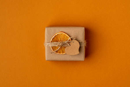 Craft gift package on orange background. Handcrafted cardboard box in wrapping paper and adornment.の写真素材