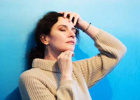 Artistic portrait of a woman with dark hair, closed eyes and hands on her faceの写真素材