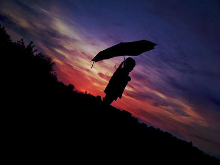 Silhouette of a woman with an umbrella on the background of a sunsetの写真素材