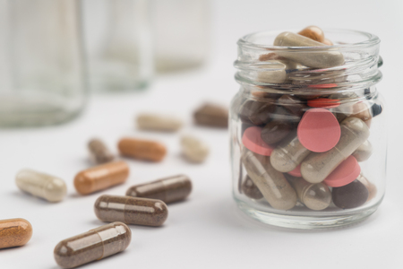 Different pills and capsules in glass jar on white background.の写真素材