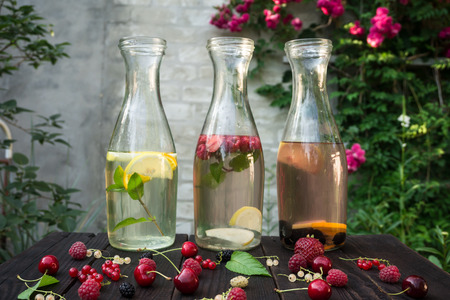 Three glass bottles with drink of mint and berries are on the dark boards on brick wall background