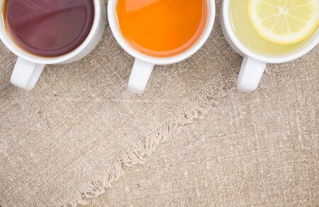 Cups with black, orange and lemon tea on the sackclothの写真素材