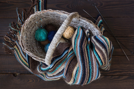 Knitted woolen scarf and yarn balls in a wicker basket on a wood